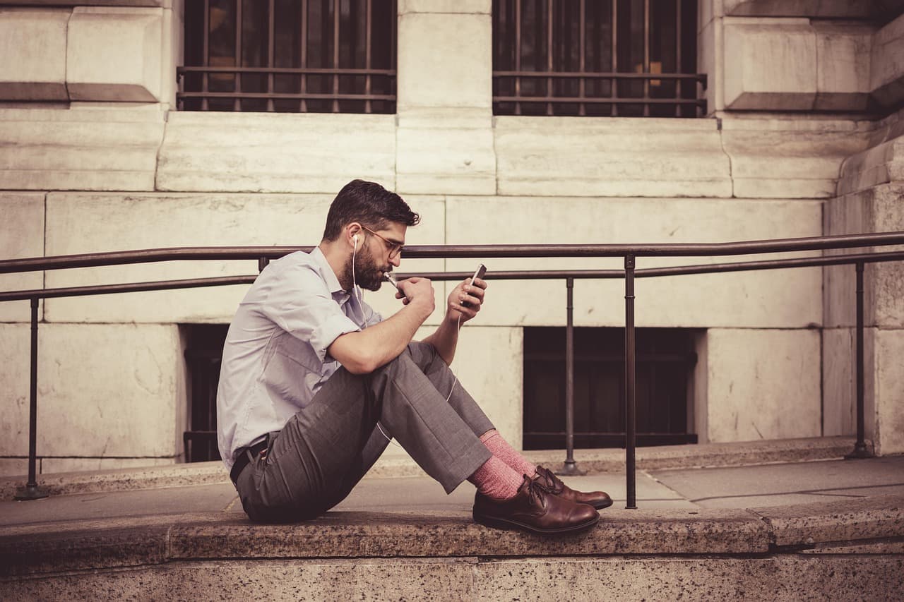 Man sitting on steps using his smartphone, illustrating Moov Money person-to-person payments to a debit card